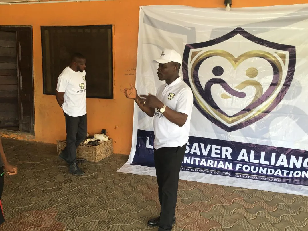 An LAHF volunteer speaks with children beside the foundation banner at City of Refuge Orphanage