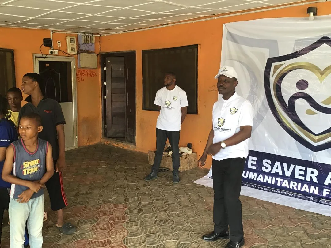 An LAHF volunteer speaks with children beside the foundation banner at City of Refuge Orphanage