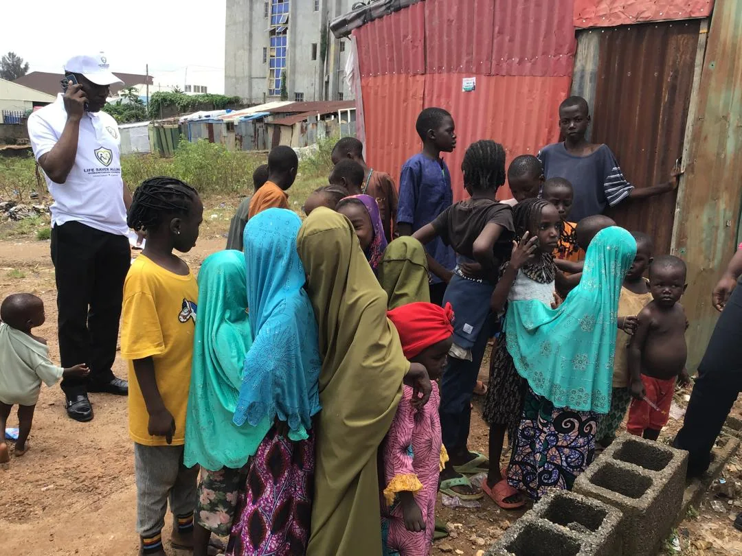 Children gather beside corrugated shelters as an LAHF volunteer joins the Crown Court Estate community visit