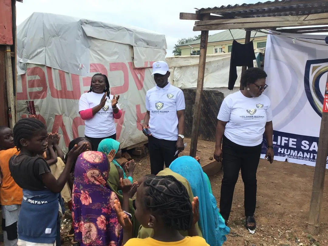 LAHF team members speak with children seated beneath a simple shelter